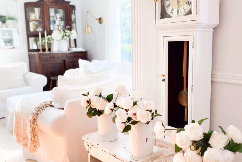 Side view of a small front entry with a vintage grandfather clock, antique white bench and 3 sap buckets with white roses