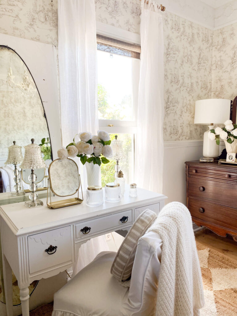 Small cottage bedroom with an antique vanity set-up with antique glass lamps and vintage perfume bottles
