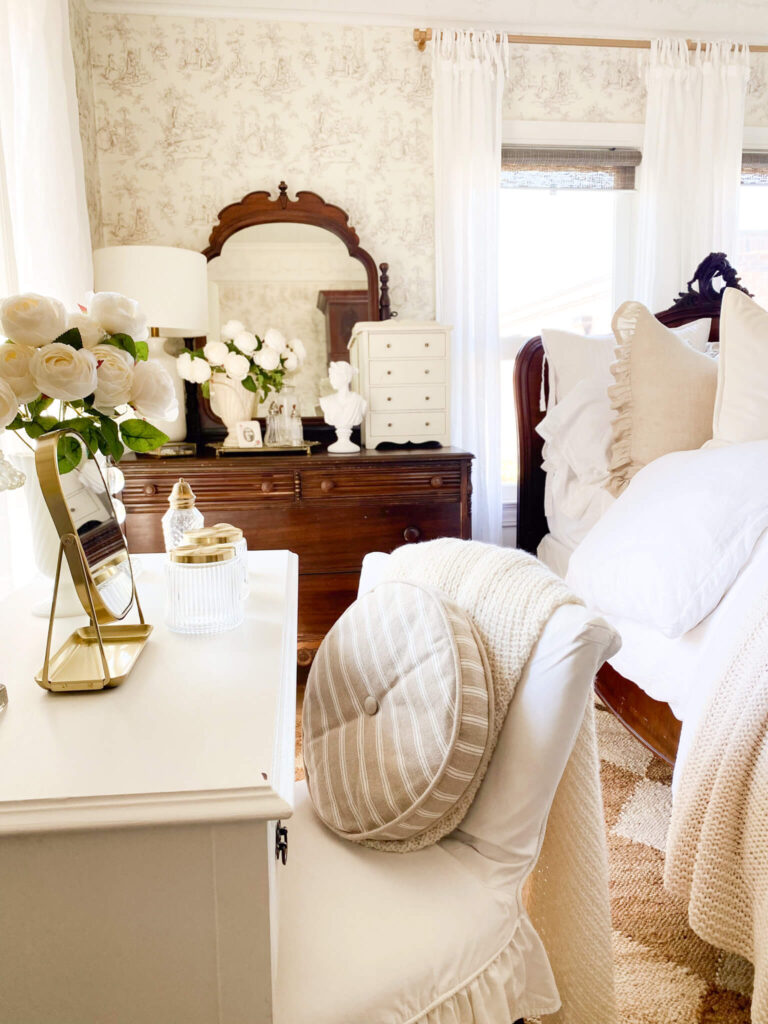 Cottage style bedroom with antique dresser with a mirror, lots of white faux roses and antique perfume bottles