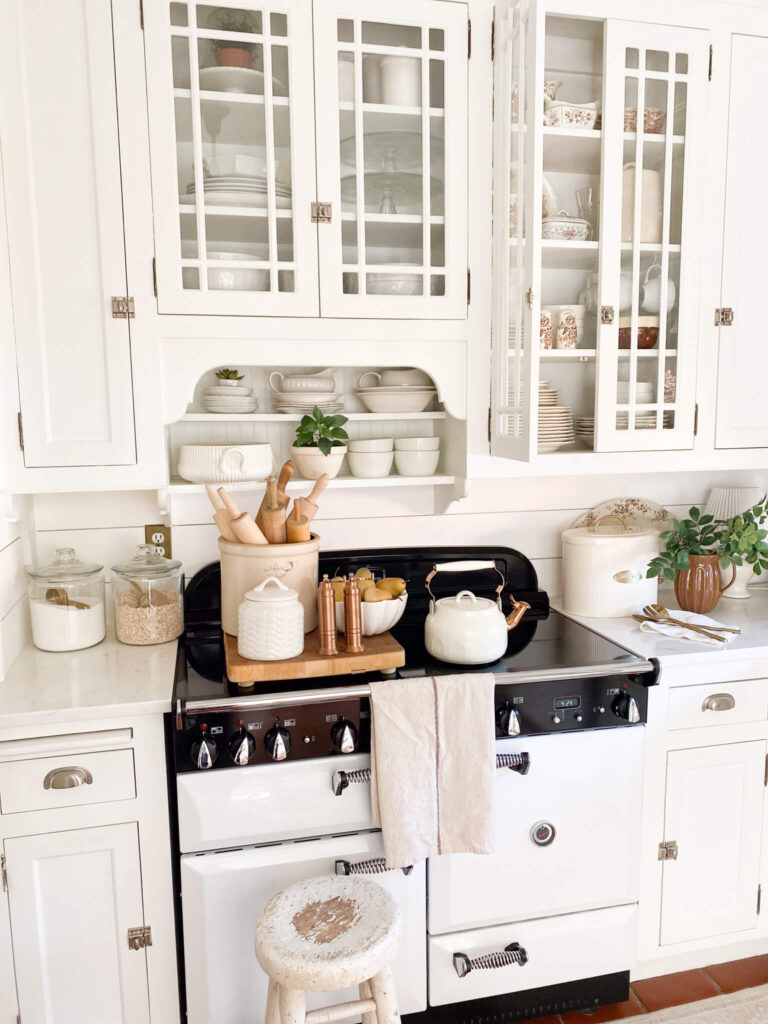 Image of a white cottage kitchen with glass cabinetry and brown ironstone collectibles