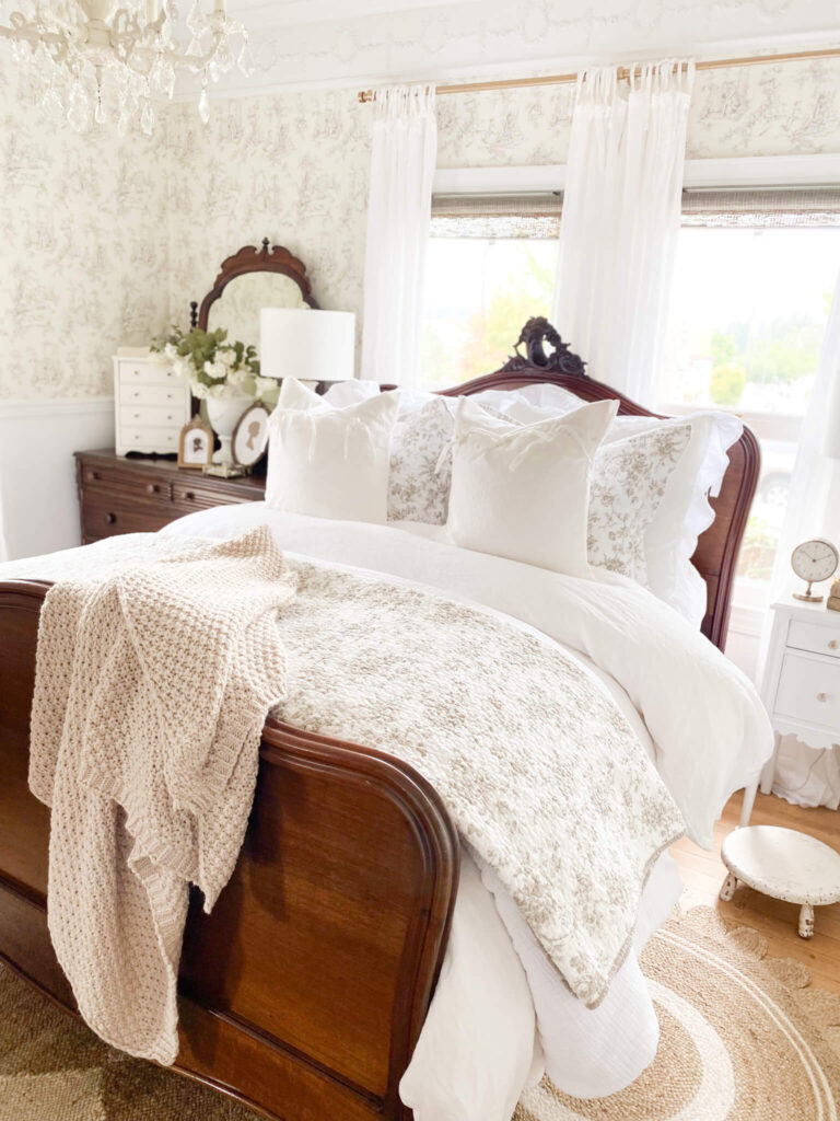 Cozy cottage vintage bed with layers of white bedding a round jute rug and antique dresser