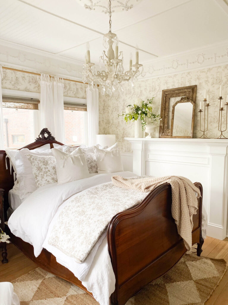 Image mage of antique bed with brown and white floral quilt and pillow shams with brown knit throw at the end of the bed