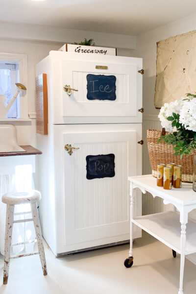 Image of a vintage style refrigerator with an antique tea cart with white spring flowers and drinks on it