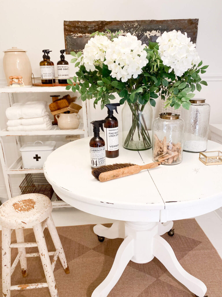 Cottage laundry room with antique table, vintage baker's rack for storage and spring floral in a large vase