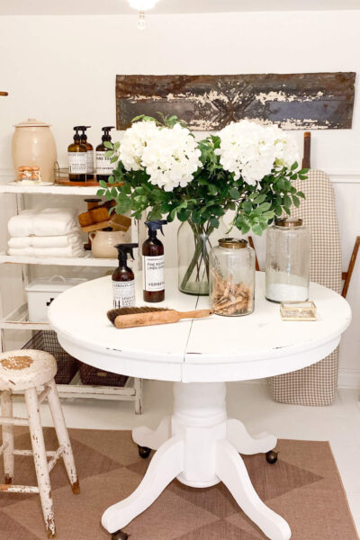 Image of a small laundry room with a round vintage table with a vase of flowers