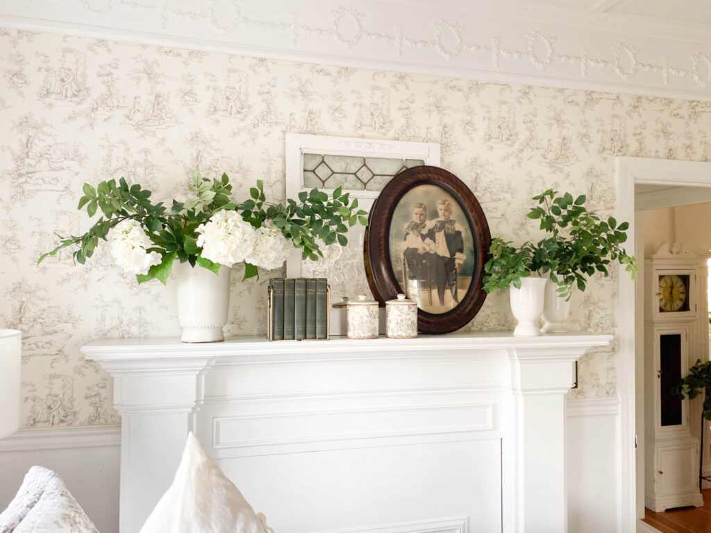 White mantel with a vintage oval frame, antique mirror, antique books and faux green stems with white spring flowers
