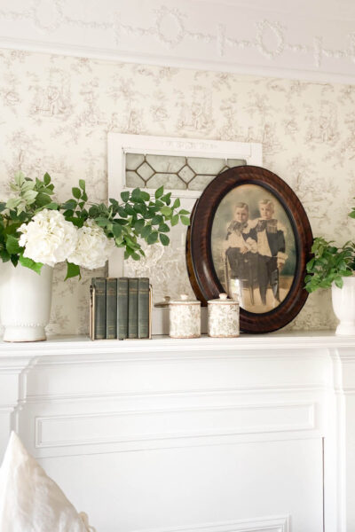 Image of a white mantel, vintage portrait with oval frame with two vases and white flowers
