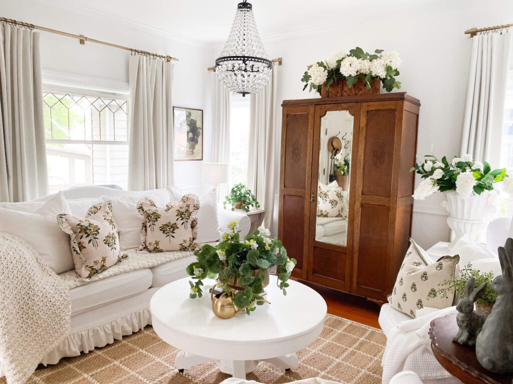 Small cottage living room with white slipcovered couch, empire chandelier, jute rug and a round vintage coffee tabe