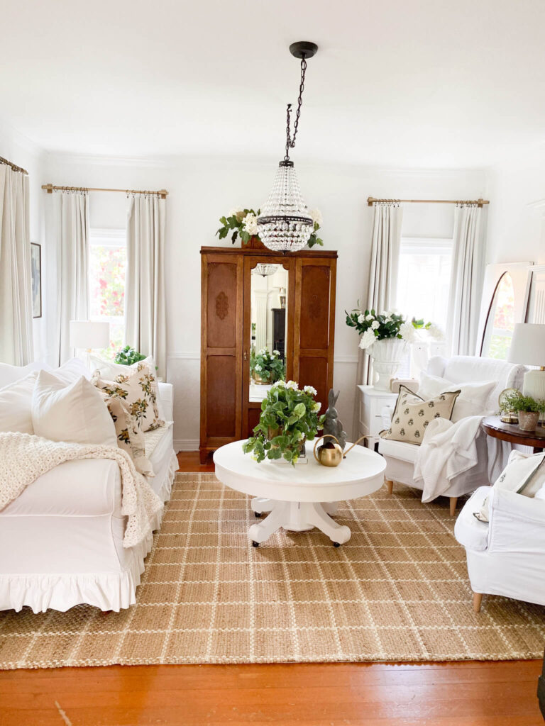 Cozy cottage living room with an antique armoire, white slipcovered couch and two white wing back chairs