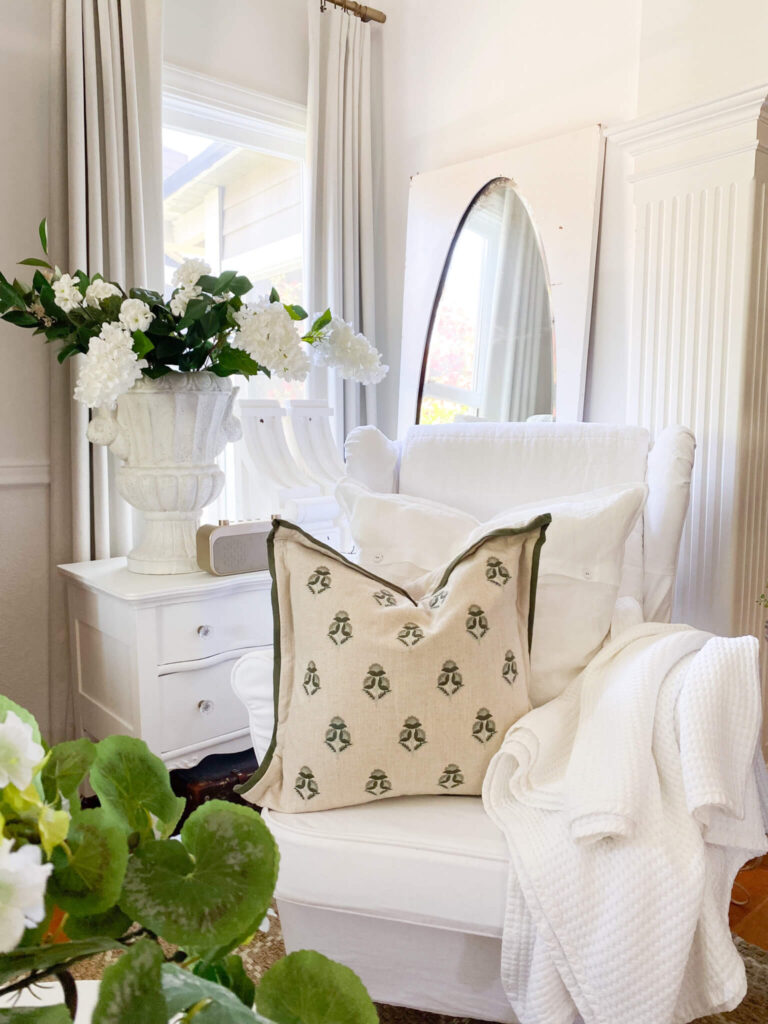 White slipcovered wing back chair with a green and cream block style pillow