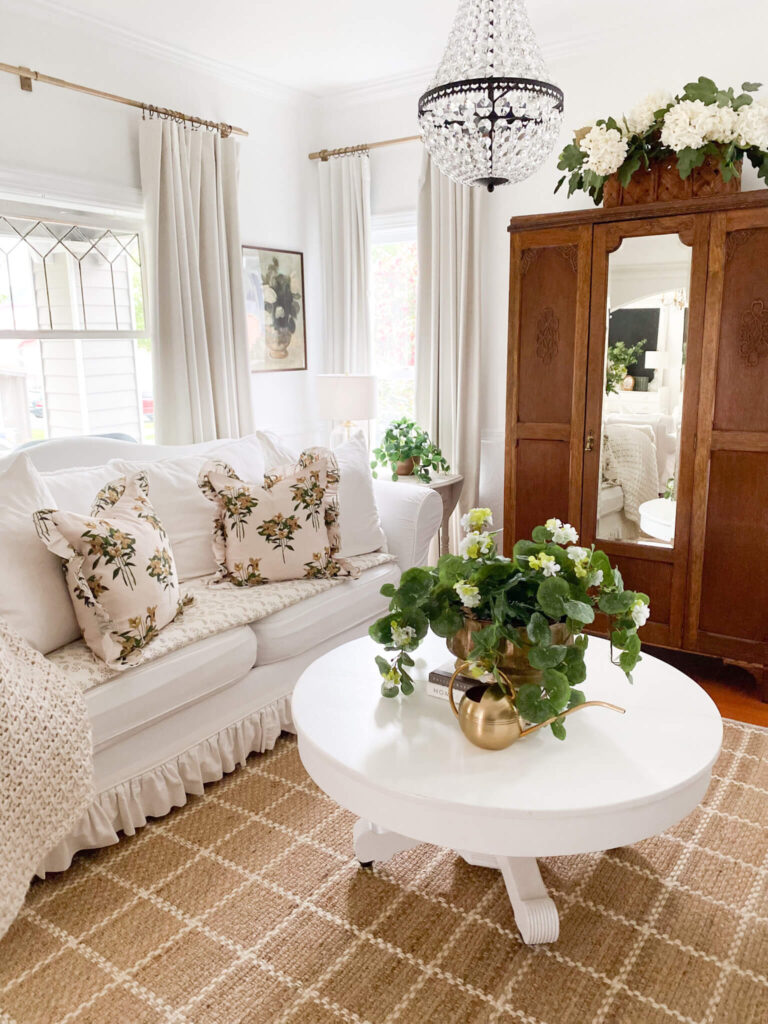 White slipcovered couch with ruffles, vintage armoire and white geranium plant tips to style a cottage living room