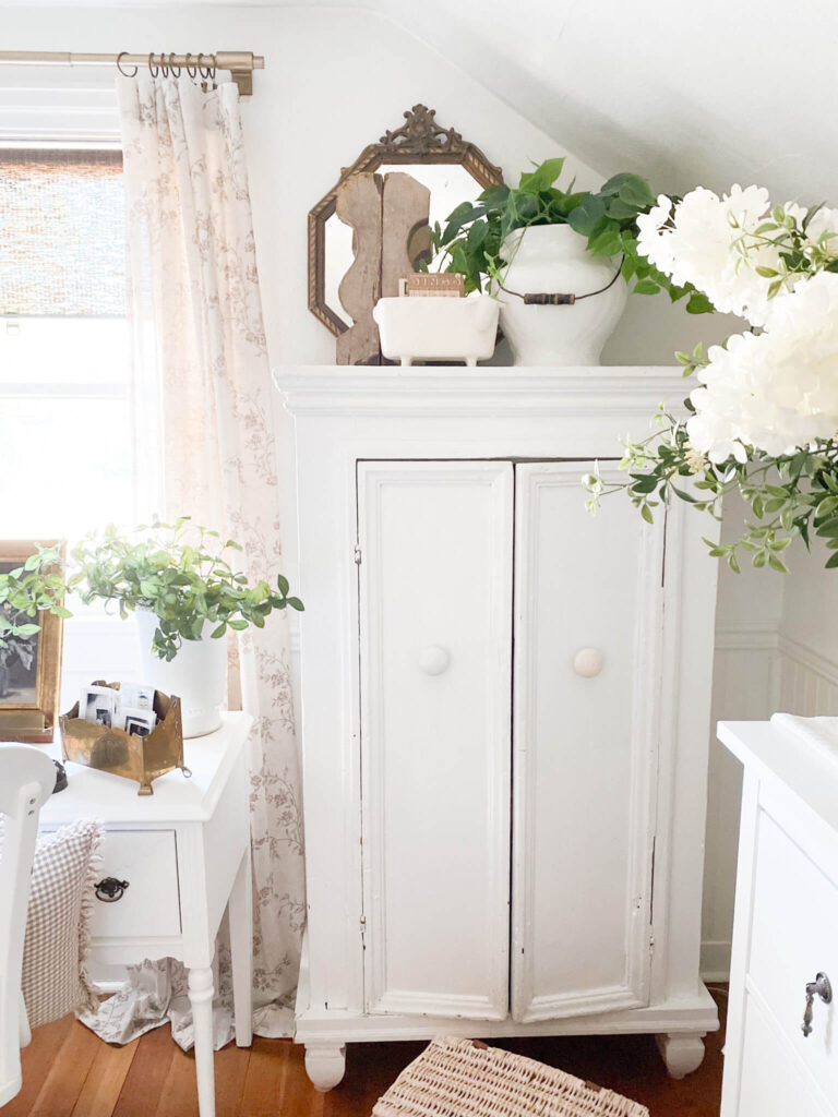 White antique linen cupboard in a cottage style bedroom with spring florals for cozy room ideas