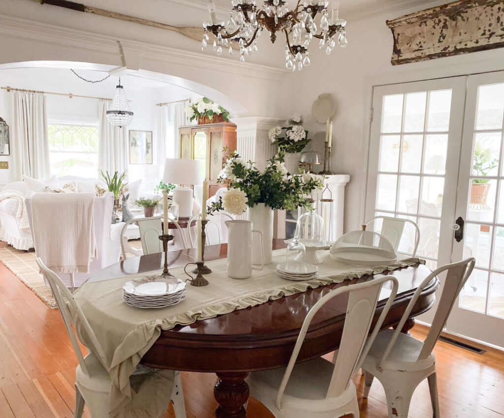 Vintage dining room with layers of white dishes, white florals, a vintage chandelier and a large antique table