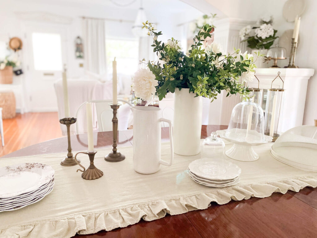 Neutrally styled farm table with ruffled table cloth, white cabbage dishes and brass candlesticks