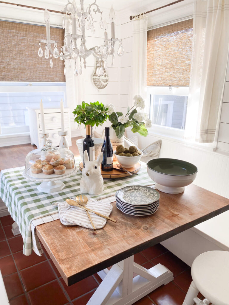 Farmhouse inspired breakfast nook with green and white floral plates, a cake plate, gingham tablecloth and bunny pitcher
