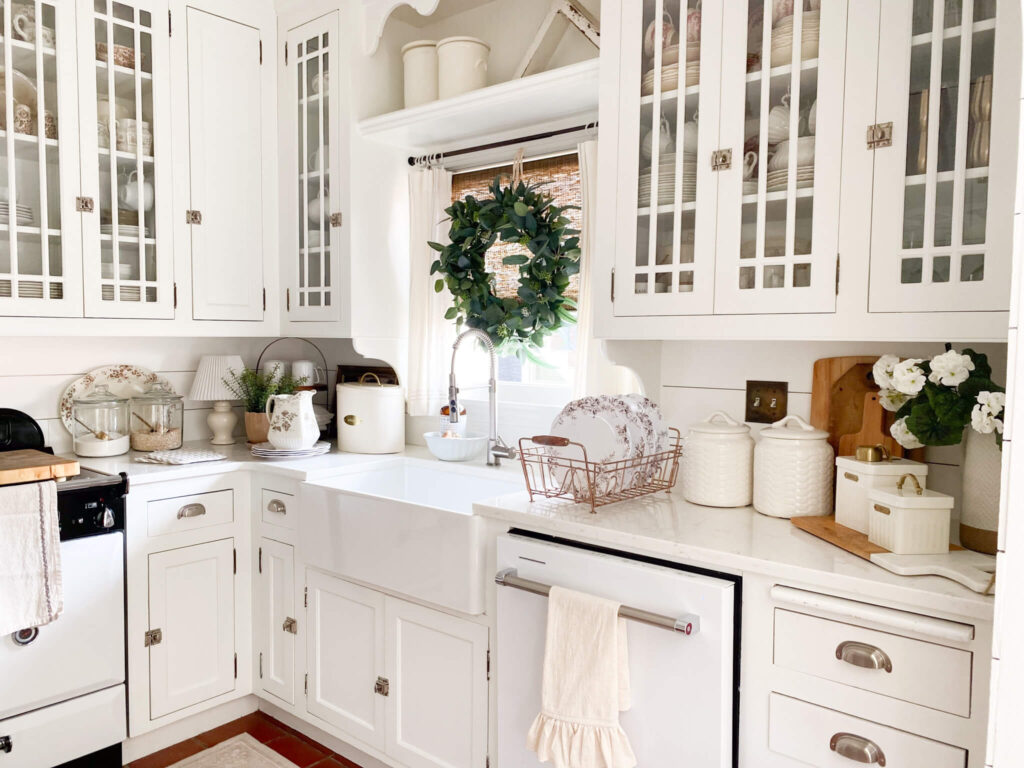White glass cabinetry, farm sink and brown transferware melamine plates for a cottage kitchen