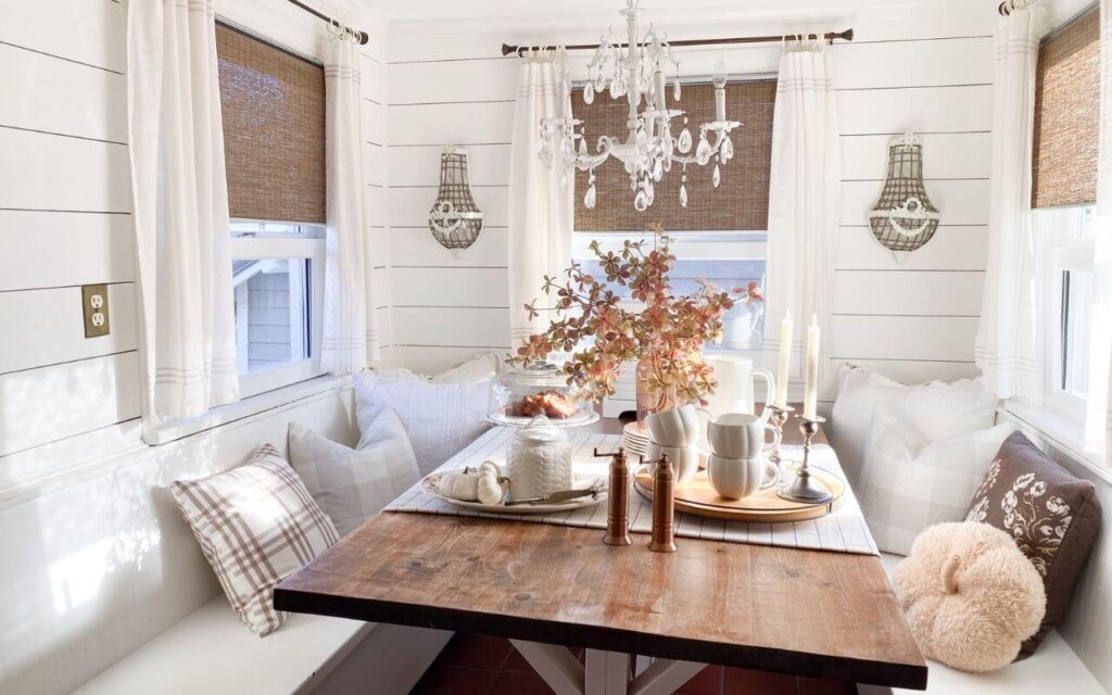 Cozy fall kitchen nook with plaid pillows, neutral pumpkins, and white shiplap walls