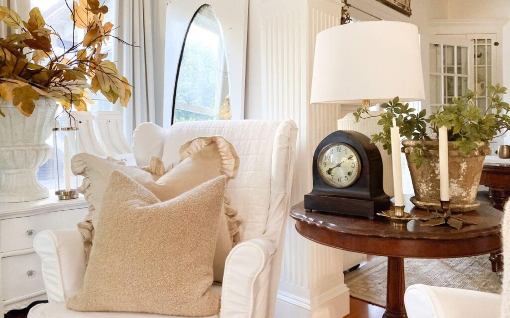 White slipcovered wingback chair with fall pillows with a vintage side table styled for fall