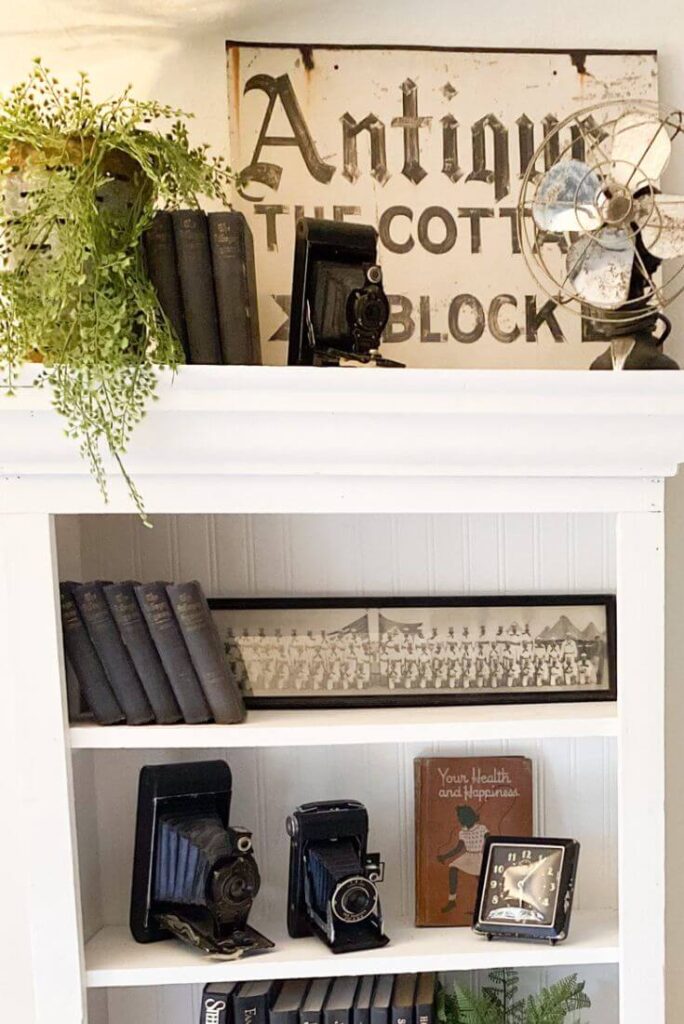 Antique cameras, vintage photos and old books styled in a white cottage bookcase
