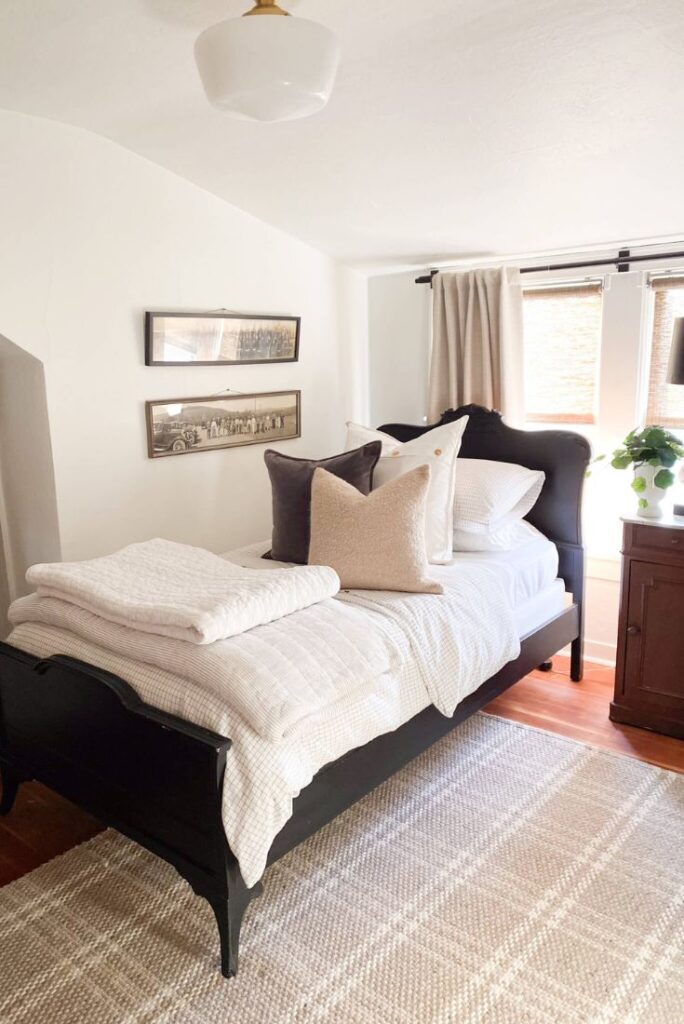 Vintage bed painted black with cozy throw pillows and white quilts for a cozy cottage guest bedroom