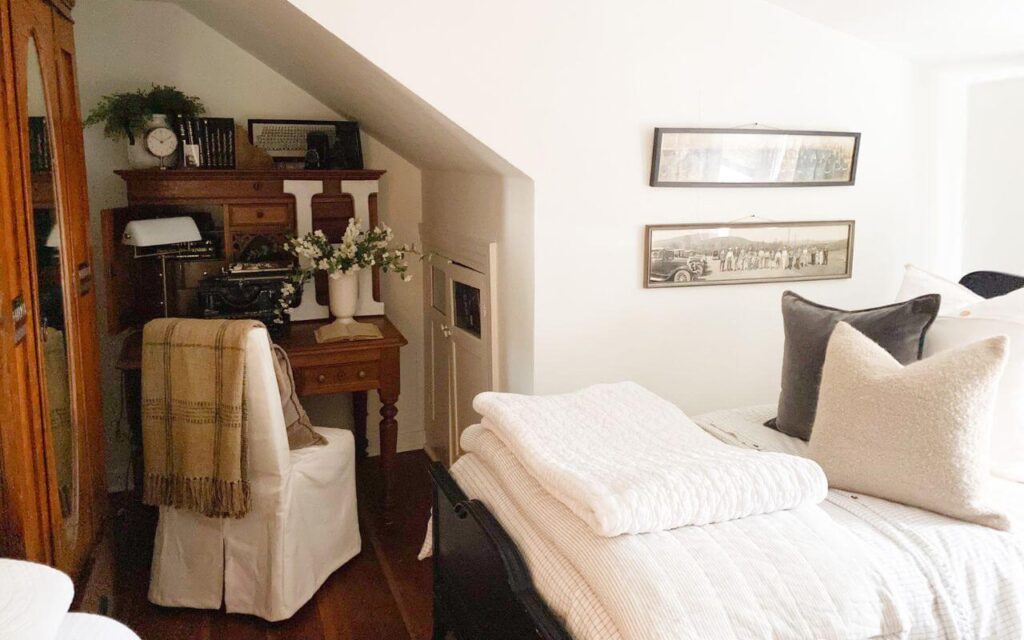 Cottage bedroom styling with an antique desk, layered antique bed and yard long military vintage photos