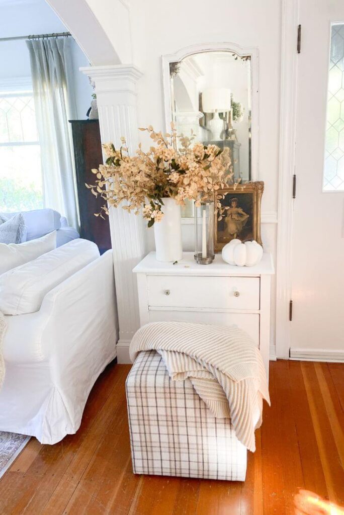 Small cottage entryway styled for fall with plaid ottoman, gold faux stems and vintage art.