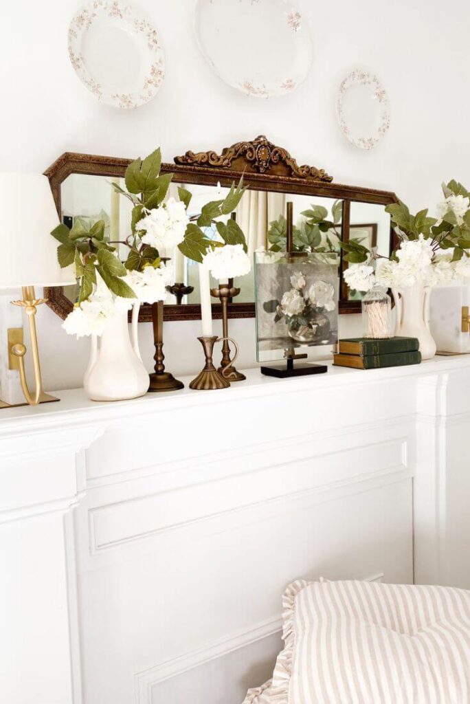 Pair of antique vases filled with greenery on mantel beside stacked books.