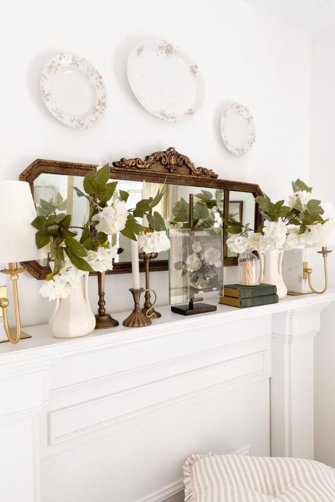 Antique mirror above white cottage mantel styled with brass candelabras and floral artwork