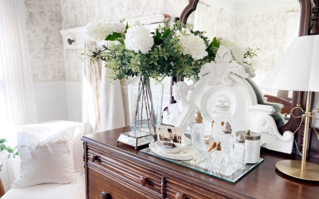 Close up of antique dresser styled with a large vase with white flowers and antique bottles.