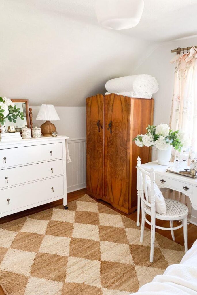 Cottage guest bedroom with antique armoire, ruffled white quilt and white dresser.