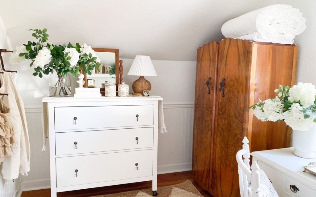 Small bedroom in a white cottage with white dresser and small antique armoire