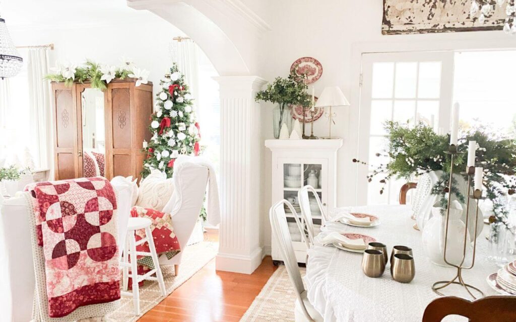 Wide view of a Christmas dining room table styled with vintage red transferware, brass candlesticks, and simple greenery