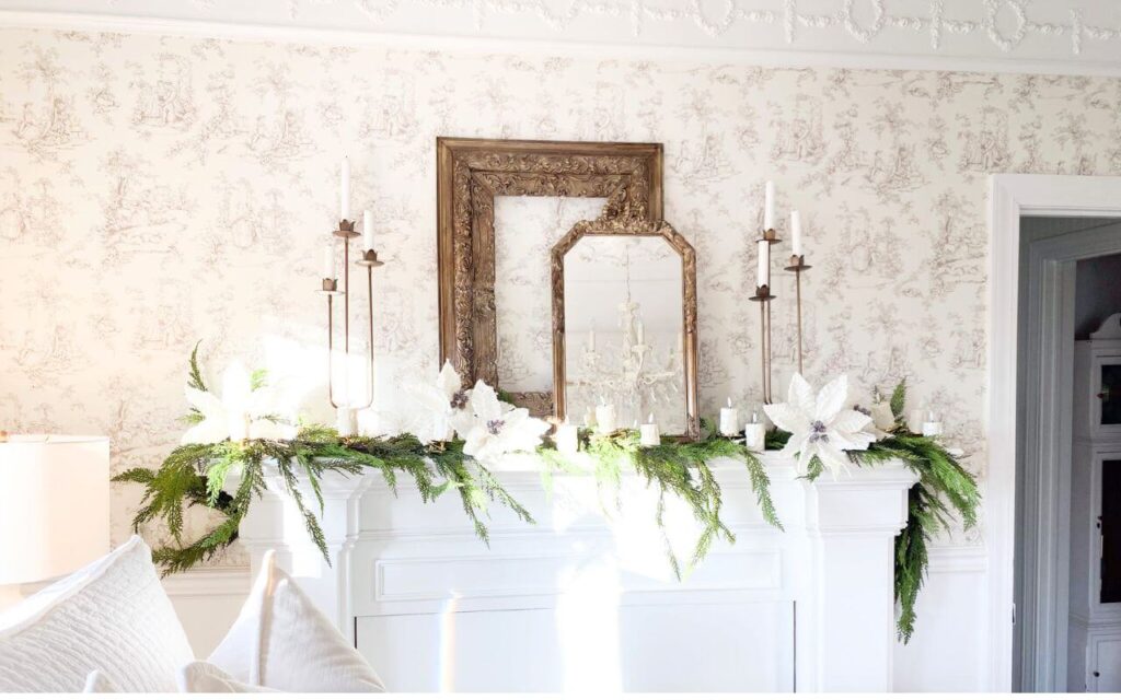 Bedroom mantel decorated with layered gold frames, brass candelabras, white poinsettias, and faux greenery for a cozy Christmas look.