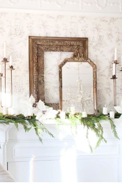 Bedroom mantel decorated with layered gold frames, brass candelabras, white poinsettias, and faux greenery for a cozy Christmas look.