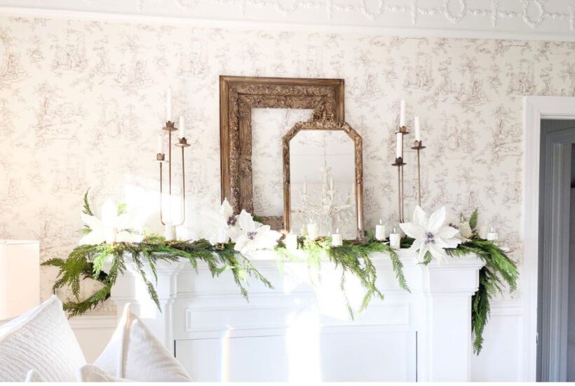 Bedroom mantel decorated with layered gold frames, brass candelabras, white poinsettias, and faux greenery for a cozy Christmas look.