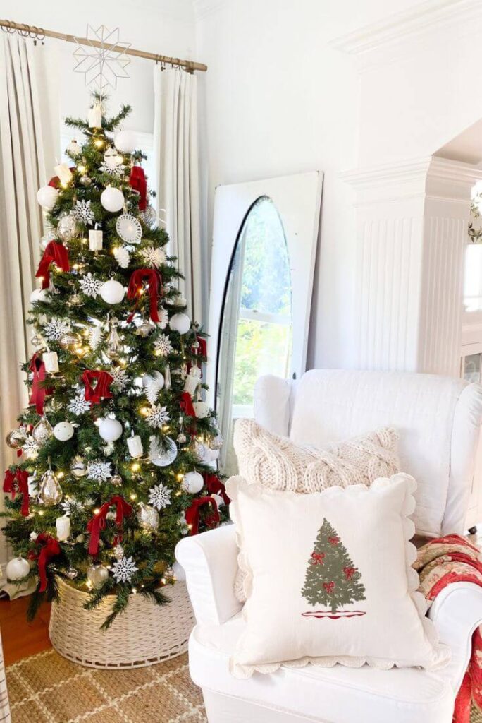 Christmas tree with red velvet bows next to a slipcovered white wingback chair.