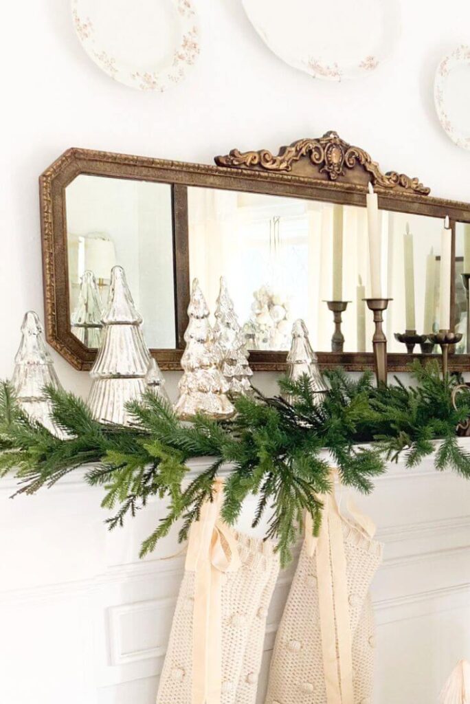 Vintage mirror above a living room mantel decorated with Christmas garland, stockings, and mercury glass trees.