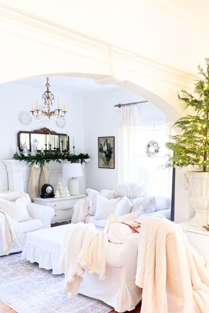 White cottage living room with white mantel styled for Christmas with faux garland and brass candelabras