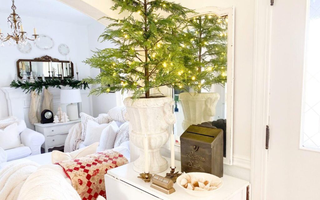 Pre-lit Christmas tree on a small table, adding soft glow to a cottage style Christmas entryway.