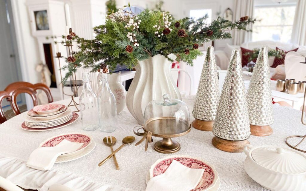 Vintage Christmas dining room table featuring red transferware dishes, ironstone pitchers, and faux greenery centerpiece