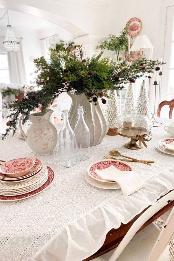 Close-up of a Christmas table styled with red transferware dishes, brass candlesticks, and greenery