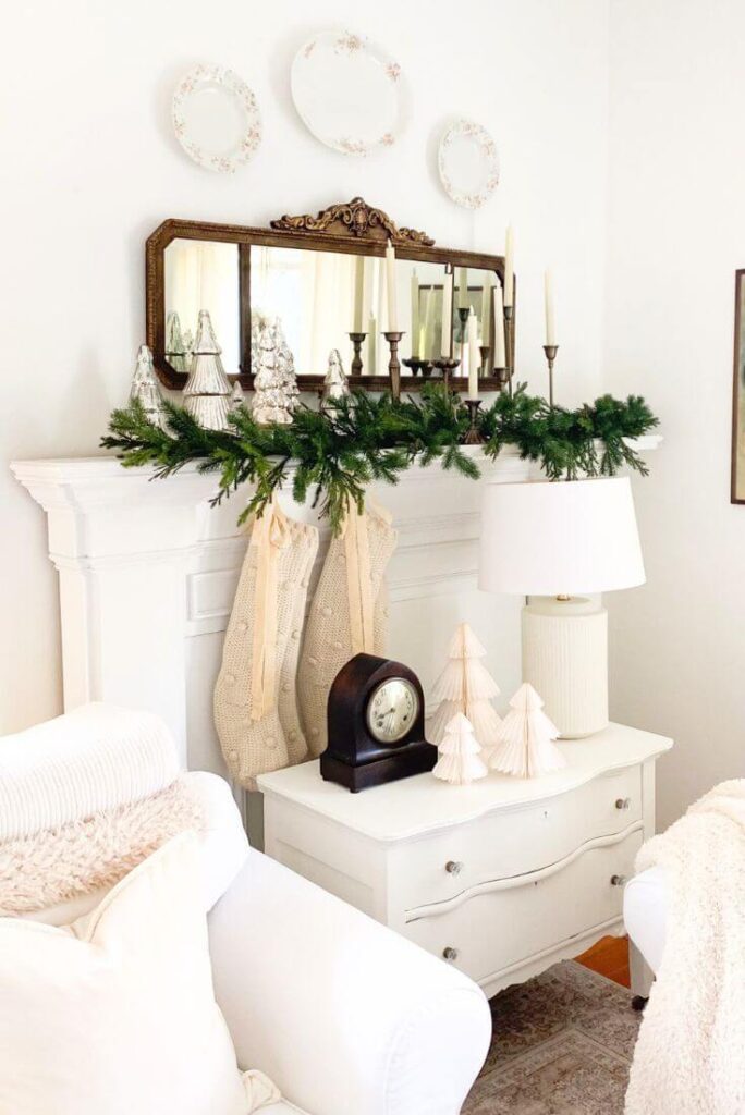 Living room Christmas mantel styled with a vintage mirror, brass accents, knit stockings, and greenery.