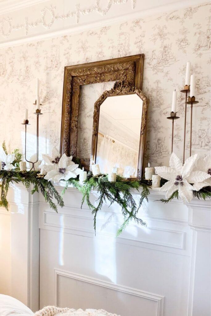 Close-up of brass candelabras and white poinsettias styled on a vintage bedroom mantel with gold frames.