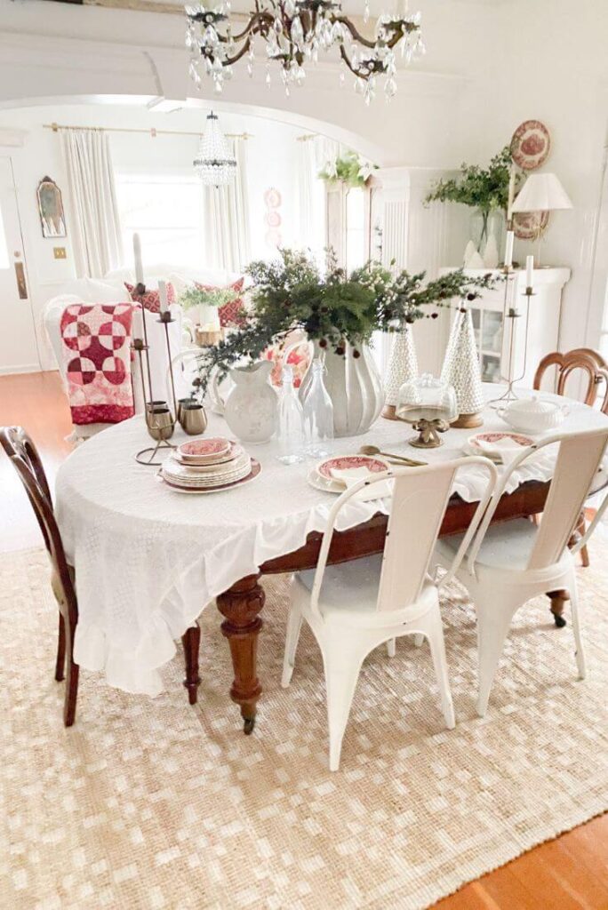 Cottage-style Christmas dining room decor with a ruffled tablecloth, vintage red dishes, and soft holiday layers