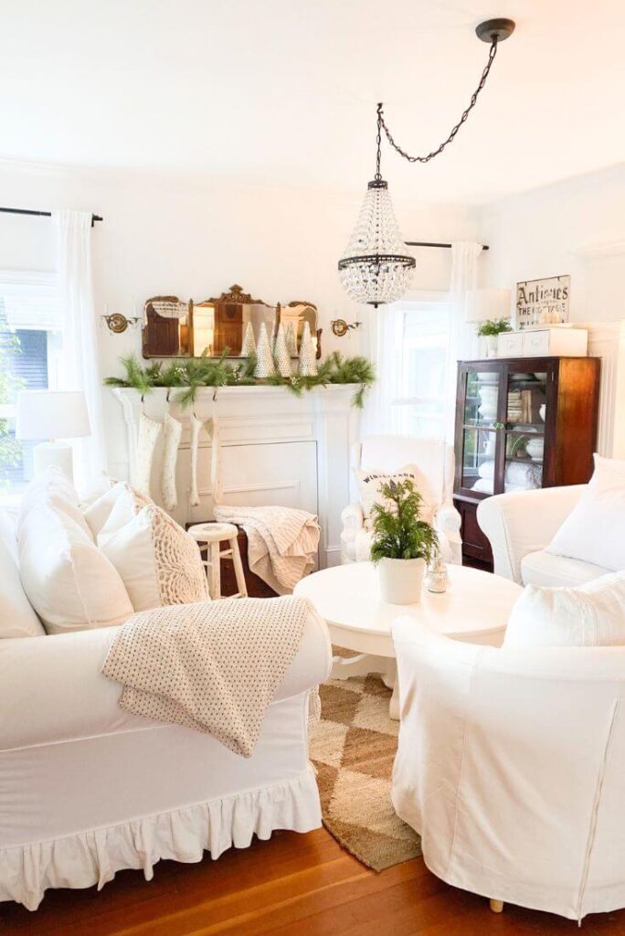 Wide view of a cozy living room with a Christmas mantel featuring mercury glass trees, knit stockings, and winter greenery.