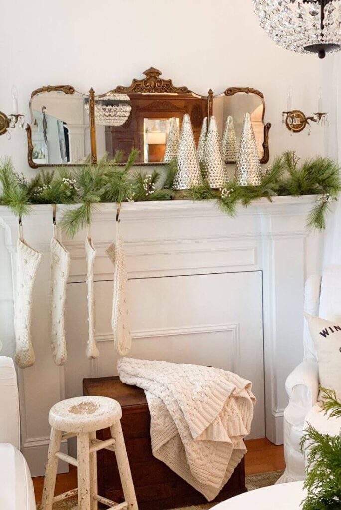 Living room Christmas mantel with garland, a gold antique mirror, and mercury glass trees.
