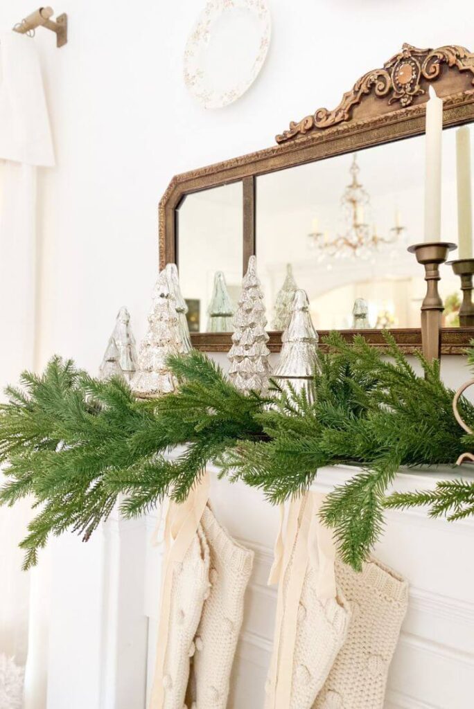 Close-up of knit Christmas stockings hanging from a mantel styled with brass accents and winter greenery.