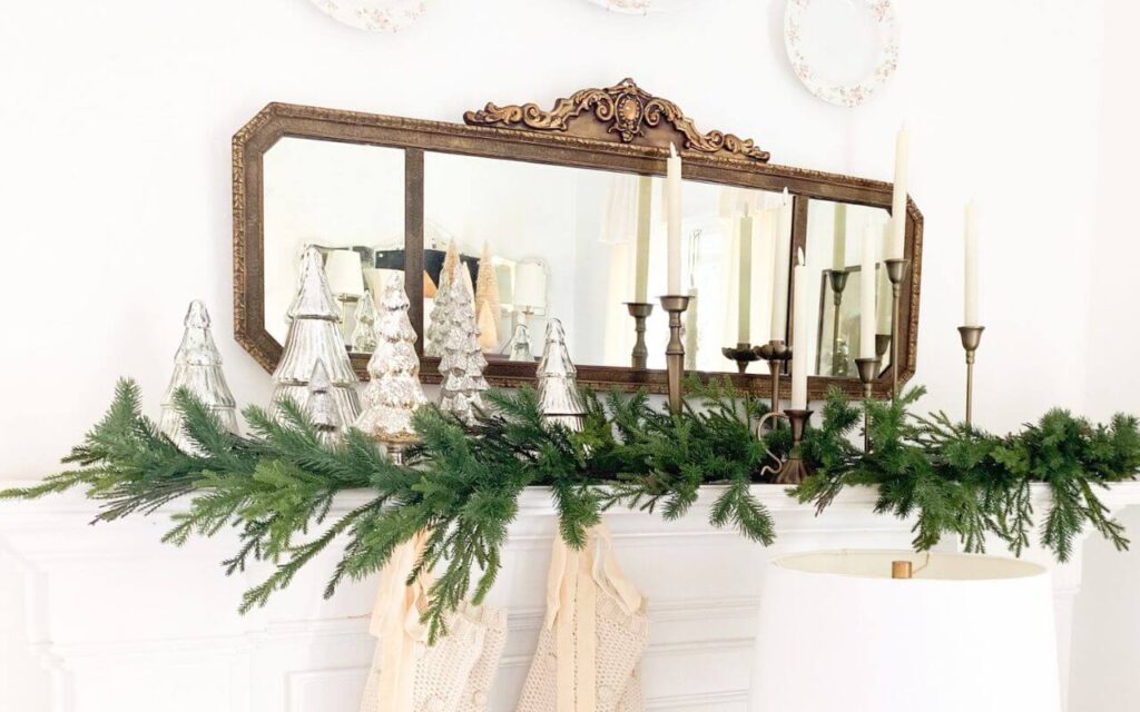 Antique gold mirror over a white fireplace mantel styled for Christmas with garland, knit stockings, velvet ribbon and brass candelabras.