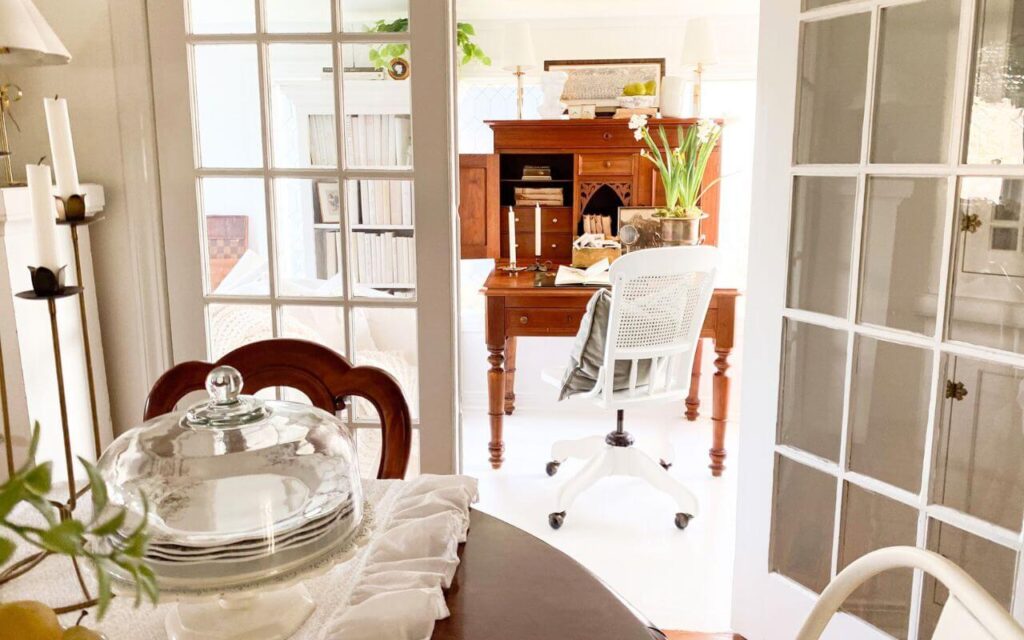 Small home library created in a sunroom with antique desk and bookcases