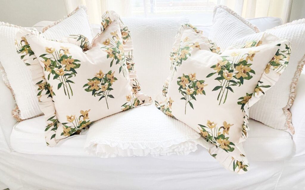Close up of yellow floral ruffled pillows and a white ruffled coverlet on a white slipcovered couch.